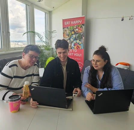 Drei EatHappy Mitarbeitende sitzen gemeinsam am Tisch mit Laptops und unterhalten sich freundlich