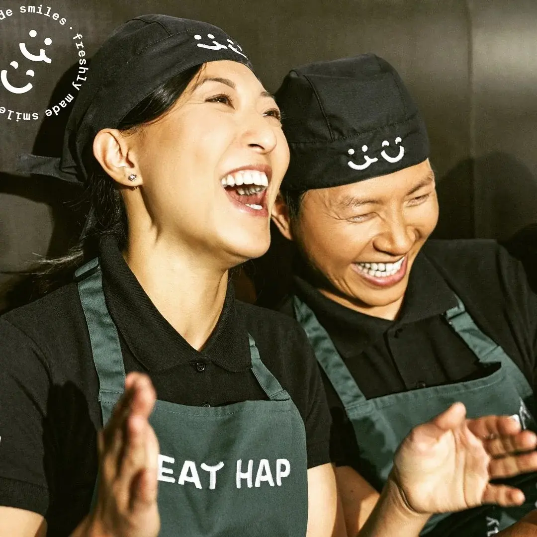 Zwei EatHappy Mitarbeiterinnen lachen gemeinsam in Arbeitskleidung und vermitteln Freude und Teamgeist